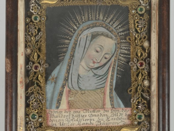 Devoční obrázek s Madonou z Landshutu, malba na papíru a textilní aplikace, po obvodu čtyři ostatky světců, výzdoba z dracounu, bulionu a sklíček, Bavorsko (Landshut ?), 2. polovina 18. století, 23,5 x 19 x 3,5 cm.
