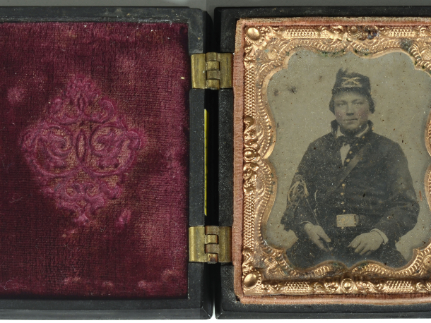 Sedící voják, kolorovaná nestandardní ambrotypie, adjustace typ: Union Cases USA - používáno od roku 1854, uložena v černé plasticky zdobené kazetě, v oválu orel + nápis CONSTITUTION AND THE LAWS